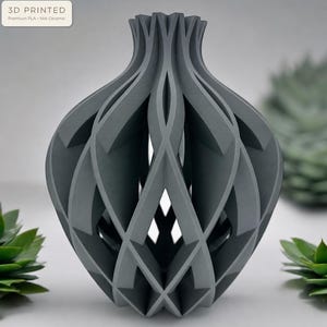 May include: A dark gray 3D printed vase with a complex, open-work geometric structure. The object features a series of interlocking, curved vertical fins that create a hollow, cage-like form. A label in the corner reads 3D PRINTED Premium PLA - Not Ceramic.