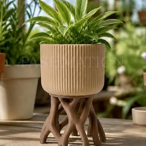 May include: A 3D printed plant pot with a ribbed, light tan exterior, supported by a brown, branch-like base. The pot contains a green leafy plant. A label in the upper left corner reads: 3D PRINTED Premium PLA - Not Ceramic.