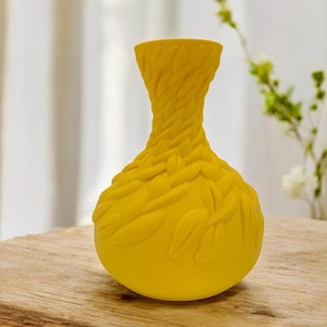May include: A yellow ceramic vase with a textured, woven design. The vase has a round body and a narrow neck.