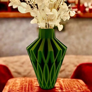 May include: A green geometric vase with a unique, intricate design. The vase is filled with white dried flowers.