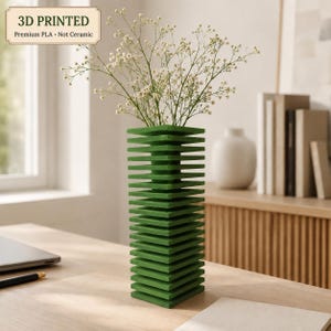 Könnte beinhalten: Eine grüne 3D-gedruckte Vase aus Premium-PLA, keine Keramik, mit einem gestapelten, quadratischen Etagendesign. Die Vase enthält einen Strauß kleiner weißer Blumen und zeigt in der oberen Ecke den Text 3D PRINTED Premium PLA - Not Ceramic.