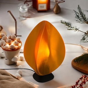 May include: A modern, orange, flame-shaped table lamp with a black base. The lamp is lit and casting a warm glow.