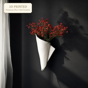 May include: A white 3D printed wall vase made of PLA, not ceramic, shaped like a folded cone. The vase holds a cluster of small red flowers. A label in the corner reads: 3D PRINTED Premium PLA • Not Ceramic.