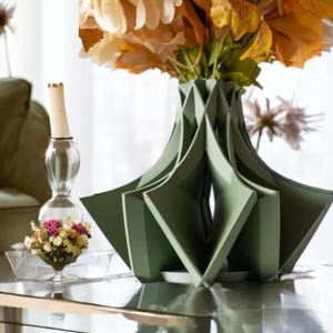 May include: A green geometric ceramic vase with a unique, folded design. The vase is filled with dried flowers in shades of yellow and brown.