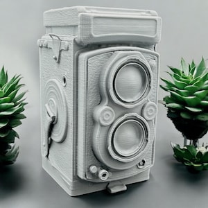 May include: A gray, vintage-style camera with a detailed, textured surface. The camera features two prominent lenses, a top viewfinder, and various dials and levers. The design mimics a classic twin-lens reflex camera, perfect for photography enthusiasts or as a decorative piece.