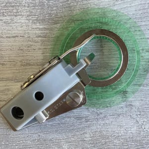 May include: A sewing machine attachment with a gray plastic body and a silver metal base. A green transparent circular guide is attached to the device. The device is labeled "M.S. STAR".