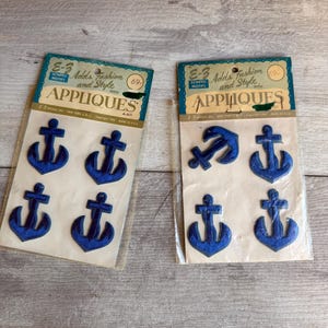 May include: Two packages of blue anchor appliqués. Each package has a vintage design with the text "E-3 Adds Fashion and Style with Appliques". The appliqués are in various sizes and shapes.