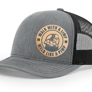 May include: A gray and black trucker hat with a brown patch that says "Walk with a limp, weld like a pimp". The patch features a silhouette of a welder.