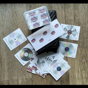 May include: A collection of CDs and stickers with a 90s theme. The CDs are silver with white cardstock sleeves. The stickers have a 90s graphic design. The text on the CDs includes "Jolene's 90s CD Jams" and "Country".