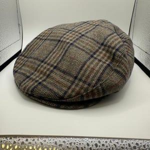 May include: A brown plaid flat cap with a rounded crown and a small, stiff brim. The cap features a classic pattern in shades of brown, blue, and red. This style of hat is often associated with traditional or vintage fashion.