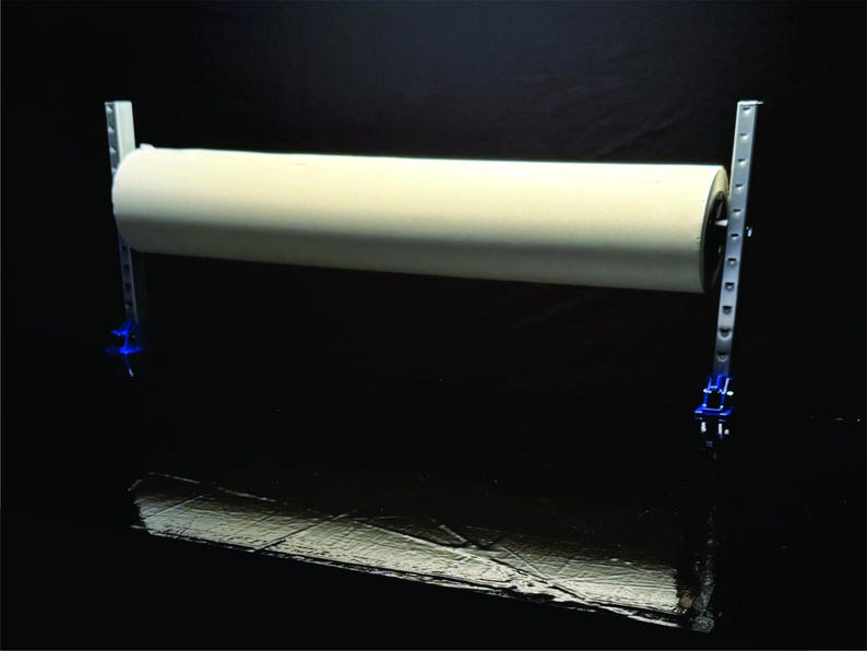 May include: A white roll of paper is mounted on a metal stand with blue clamps. The stand has a silver finish and is designed to hold a roll of paper.