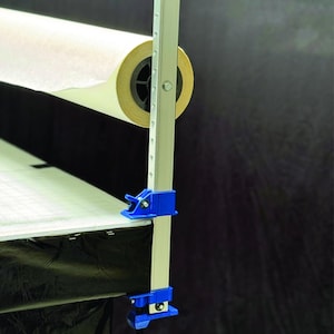 May include: A white paper roll is mounted on a silver metal stand with a blue clamp. The stand is attached to a black surface with a blue clamp.