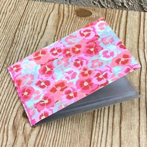 May include: A pink and red floral patterned photo album with clear plastic sleeves for holding photos.