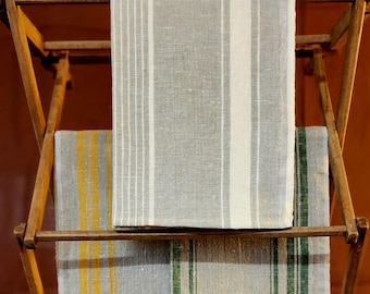 May include: Two striped linen tea towels hanging on a wooden drying rack. The top towel has white stripes and the bottom towel has yellow and green stripes.