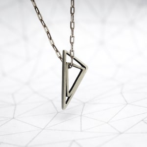Puede incluir: Un collar de plata con un colgante geométrico que presenta dos triángulos superpuestos.