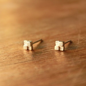 May include: A pair of silver stud earrings with a geometric design. Each earring features a small, square-shaped piece with four smaller squares arranged in a cross pattern.