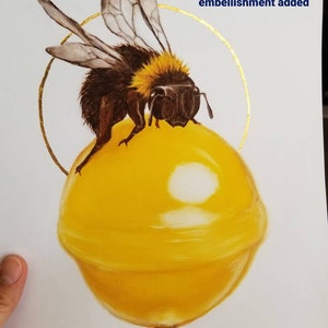 Puede incluir: Una piruleta amarilla con una abeja sobre ella. La piruleta tiene un adorno de hoja de oro alrededor.