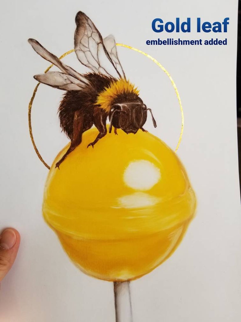 Puede incluir: Una piruleta amarilla con una abeja sobre ella. La piruleta tiene un adorno de hoja de oro alrededor.