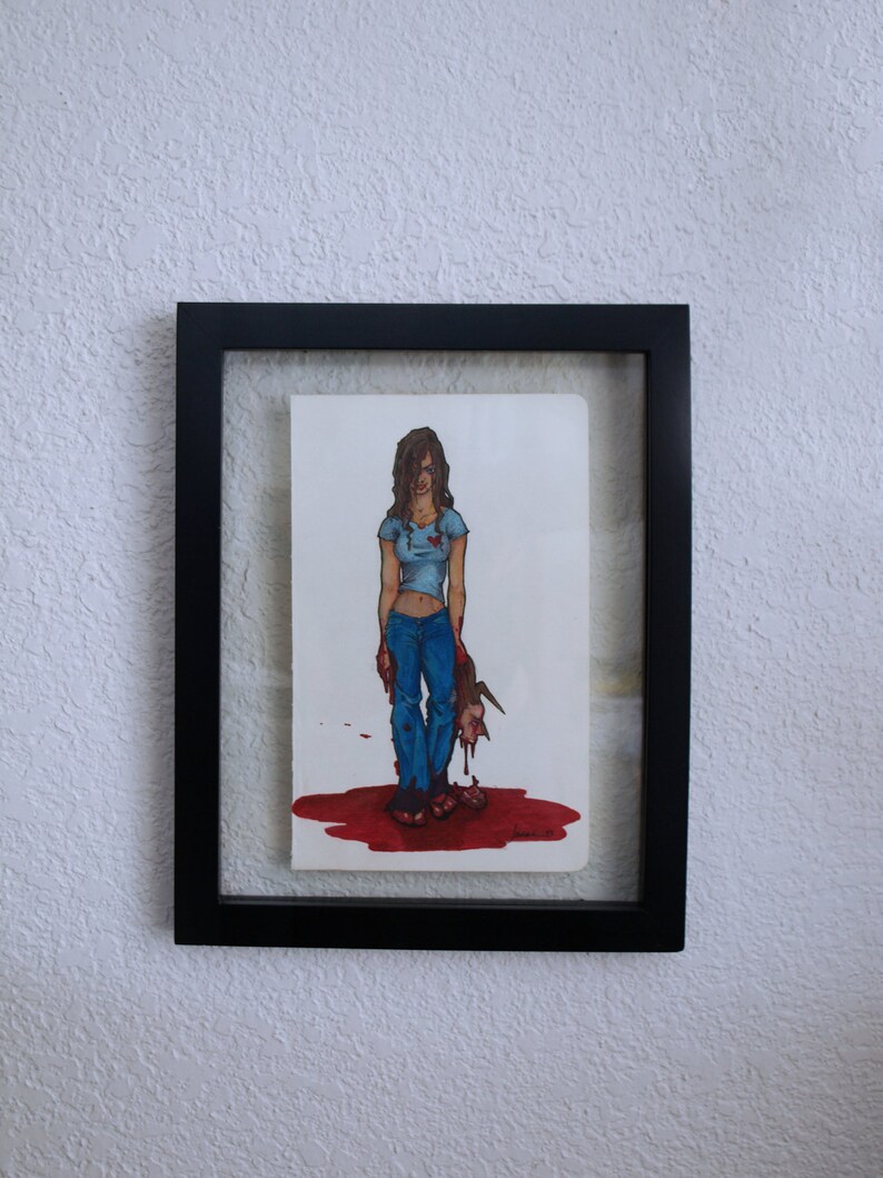 Puede incluir: Un dibujo enmarcado de una mujer con jeans azules y una camisa azul de pie en un charco de sangre con una cabeza cortada a sus pies.