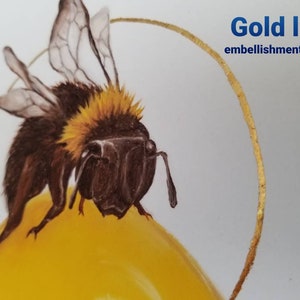 Puede incluir: Primer plano de un abejorro con pelaje marr&oacute;n y amarillo, posado sobre una superficie amarilla. El abejorro tiene alas transl&uacute;cidas y est&aacute; rodeado por un adorno de hoja de oro.