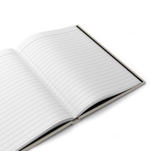 May include: An open notebook with lined pages and a black cover. The notebook is lying flat on a white surface.
