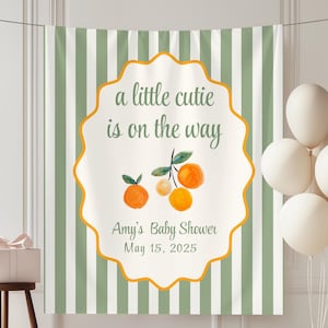 May include: A vertical fabric banner featuring sage green and white vertical stripes with a central scalloped white emblem. The text reads a little cutie is on the way, Amy's Baby Shower, May 15, 2025, accompanied by watercolour orange illustrations.