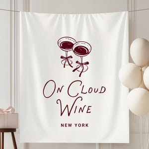 May include: A white fabric banner featuring a dark red graphic of two wine glasses tied with ribbons. Below the glasses, the text reads "On Cloud Wine" in a stylized script font, followed by the words "NEW YORK" in a simple sans-serif font.