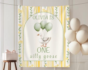 Puede incluir: Una pancarta de cumpleaños personalizada con una ilustración de acuarela de un ganso sosteniendo globos. La pancarta dice "Olivia is ONE silly goose" en escritura verde. El fondo es blanco con rayas amarillas y detalles florales.