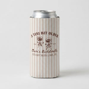 May include: A beige and white vertical striped can cooler featuring brown text that reads A TINI BIT OLDER, EST. 2026, Claire's Bachelorette, and Cedar Creek Lake, TX, with a graphic of two martini glasses tied together with a ribbon.