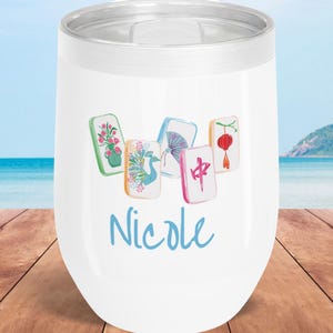 May include: White insulated wine tumbler with a silver rim, featuring a watercolor design of Mahjong tiles and the name "Nicole" in blue script. The tiles display various illustrations, including flowers, a bird, and Chinese characters.