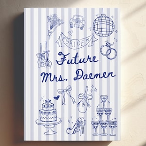 May include: A rectangular notebook with a light blue and white vertical striped cover featuring dark blue line art illustrations of a wedding cake, champagne tower, disco ball, rings, and the text "Future Mrs. Daemen" and "BRIDE".