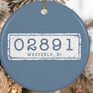 Op de afbeelding: Een ronde, blauwe keramische ornament met een wit rechthoekig ontwerp. Het ontwerp toont de nummers "02891" en de tekst "Westerly, RI" in een verweerde lettertype. Een gouden draad is bevestigd om op te hangen.
