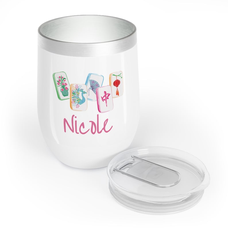 May include: White insulated tumbler with a silver rim and a clear lid. The tumbler features a watercolor design of Mahjong tiles and the name "Nicole" in pink script. The lid is off to the side.