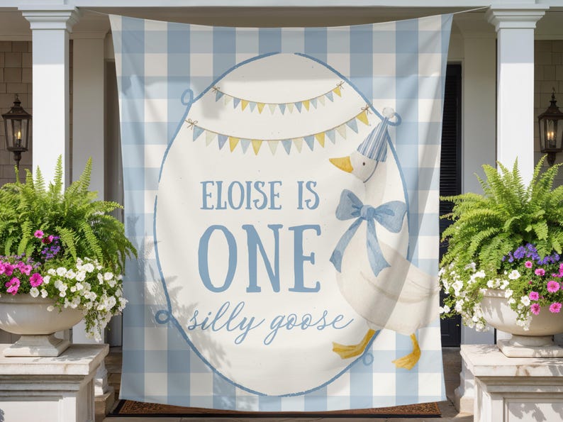 May include: A light blue and white gingham banner with an oval design featuring a goose wearing a party hat and bow. Text reads "Eloise is One silly goose". The banner is hanging on a porch.