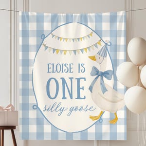 May include: A blue and white gingham backdrop with a banner that reads "Eloise is One, a silly goose." A cartoon goose wearing a party hat and bow tie is featured. White balloons and a gift box complete the scene, perfect for a first birthday.
