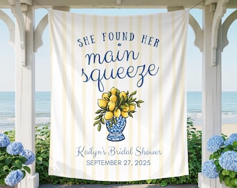May include: A white banner with yellow vertical stripes and navy blue script that reads "SHE FOUND HER main squeeze". A blue and white vase with lemons and greenery is below the text. The banner reads "Kailyn's Bridal Shower SEPTEMBER 27, 2025".