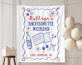 Op de afbeelding: Witte stoffen banner met een blauw en rood ontwerp. De banner leest "Kathryn's Bachelorette Weekend Lake Norman, NC" met illustraties van een fles, vlag, vuurwerk en cocktails. Witte ballonnen zijn rechts.