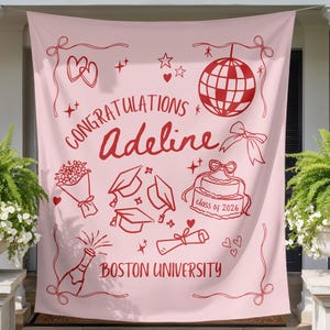 May include: A pink graduation banner with red illustrations and text. The banner says "Congratulations Adeline" and "Boston University". It features graduation caps, a cake, a disco ball, and a champagne bottle.