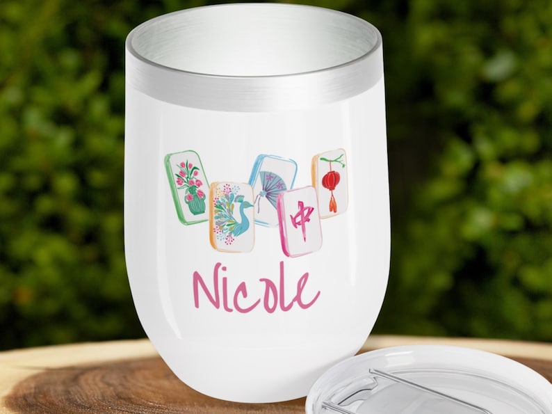 May include: White stemless wine tumbler with a silver rim, featuring a watercolor design of Mahjong tiles and the name "Nicole" in pink script. The tumbler has a lid.