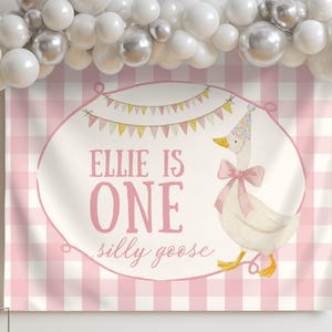 May include: A pink and white gingham backdrop with the text "Ellie is One silly goose". A watercolor illustration of a goose wearing a party hat and bow is on the backdrop. White and silver balloons are above.
