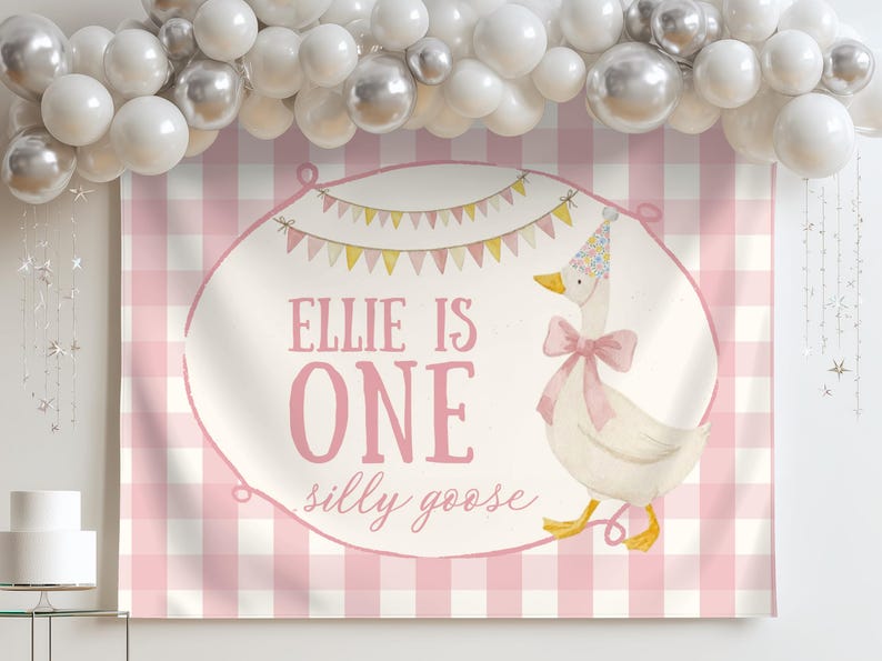 May include: A pink and white gingham backdrop with the text "Ellie is One silly goose". A watercolor illustration of a goose wearing a party hat and bow is on the backdrop. White and silver balloons are above.