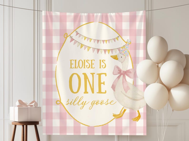 May include: A pink and white gingham backdrop with a large egg-shaped design featuring a goose illustration and the text "Eloise is One silly goose." A bundle of white balloons and a gift box are also present.