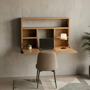 May include: A light brown, wall-mounted desk with a built-in shelf unit. The desk has a fold-down work surface and includes a laptop, a small lamp, and a potted plant. A neutral-colored chair sits in front of the desk. The desk is mounted on a gray wall.