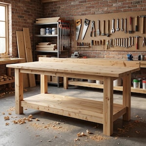 Puede incluir: Un banco de trabajo grande de madera sin terminar con un estante inferior, en un taller. El banco de trabajo es de madera clara y tiene una parte superior rectangular. El fondo presenta una pared de ladrillo, herramientas y madera.