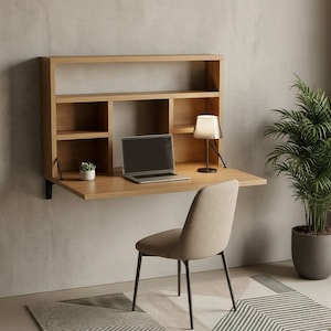 May include: A wall-mounted wooden desk with a built-in shelf unit. The desk features a laptop, a small lamp, and a potted plant. A beige chair sits in front of the desk. The desk is made of light-colored wood and is mounted on a light gray wall.