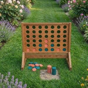Puede incluir: Un tablero de juego de cuatro en raya de madera con una cuadr&iacute;cula de agujeros circulares y acabado marr&oacute;n claro. El tablero contiene varias fichas circulares de color coral y verde azulado insertadas. Hay pilas de fichas debajo del tablero.