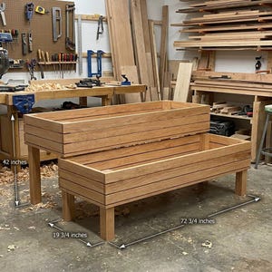 Op de afbeelding: Twee houten rechthoekige plantenbakken, de ene op de andere gestapeld, in een werkplaats. De onderste plantenbak is 184.8 cm lang, 50.2 cm breed en de bovenste plantenbak is 106.7 cm hoog. De plantenbakken zijn gemaakt van lichtbruin hout.