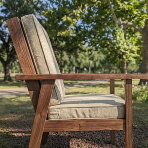 Puede incluir: Un sill&oacute;n de madera para exteriores con un coj&iacute;n verde claro. La silla tiene un acabado de madera natural y un dise&ntilde;o simple y moderno. La silla est&aacute; colocada al aire libre en un parque.