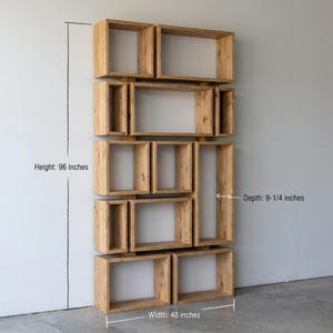 May include: A wall-mounted wooden shelving unit with a unique, geometric design. The unit is made of light-colored wood and features various rectangular and square compartments. It measures 96 inches high, 48 inches wide, and 9-1/4 inches deep.