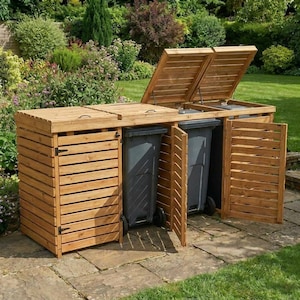 May include: A triple-bay wooden bin storage unit featuring horizontal slat walls and hinged lids. The structure is constructed from light brown wood and houses three dark grey plastic wheeled trash bins, with two lids open and two front doors open.